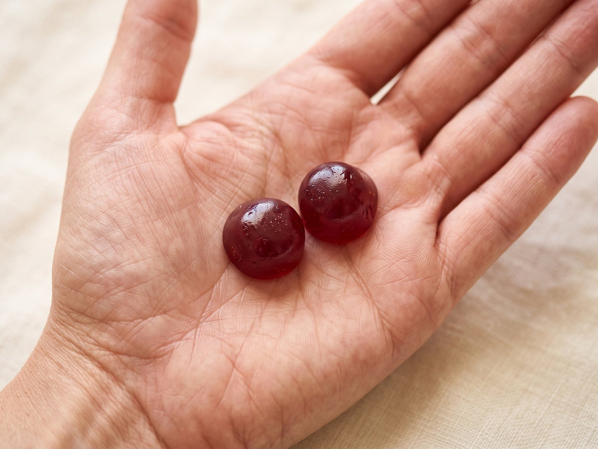 Two deep red Therapium omega-3 gummies resting on an open palm