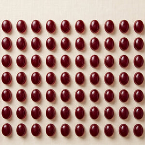 Deep red omega-3 gummies laid out in an even grid on a warm ivory surface